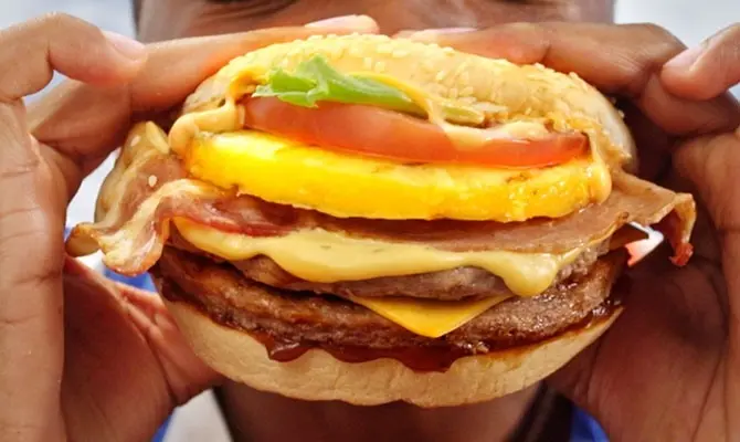 Person eating a burger with bacon and pineapple