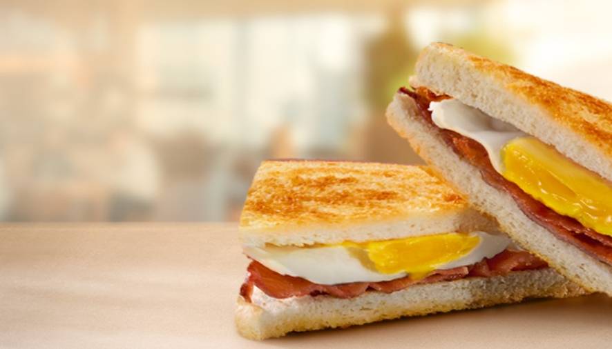 Toasted breakfast sandwich with fried egg and bacon, cut in half