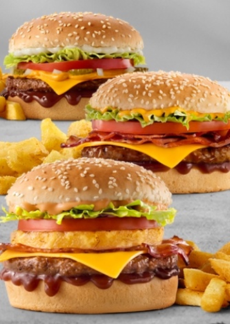 Three classic cheeseburgers with crispy bacon, onion rings, lettuce, tomato, melted cheddar cheese, barbecue sauce, sesame seed buns, and chips