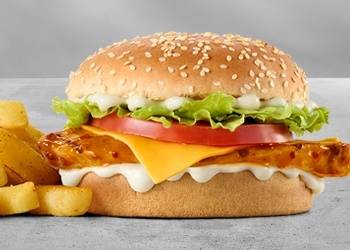 Grilled chicken cheeseburger with melted cheddar cheese, fresh lettuce, tomato slices, creamy mayo sauce, sesame seed bun, and chips
