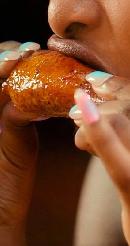 Person eating a glazed chicken wing with colorful acrylic nails, highlighting crispy fried chicken